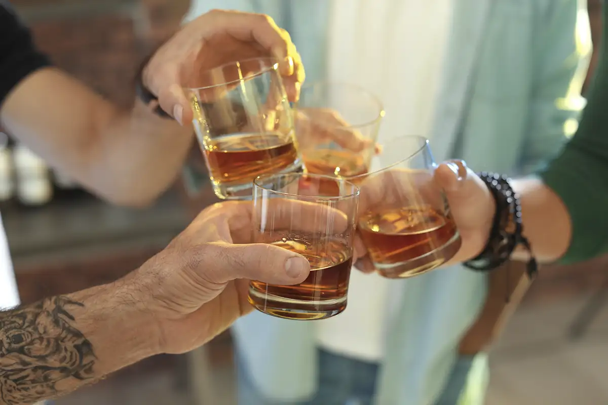 A close up of a group toasting glasses of bourbon or whiskey