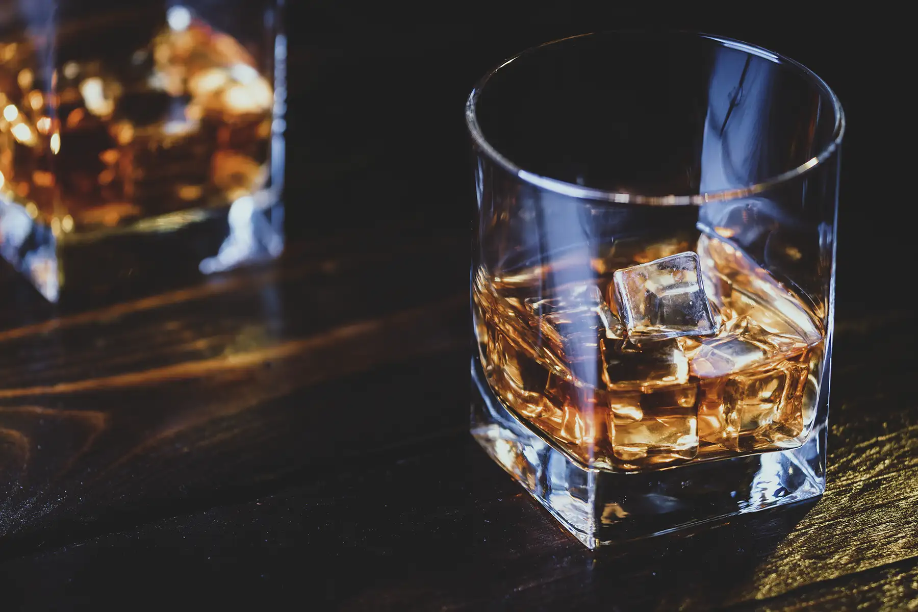 A photo of whiskey or bourbon in a glass with ice cubes, dark environment