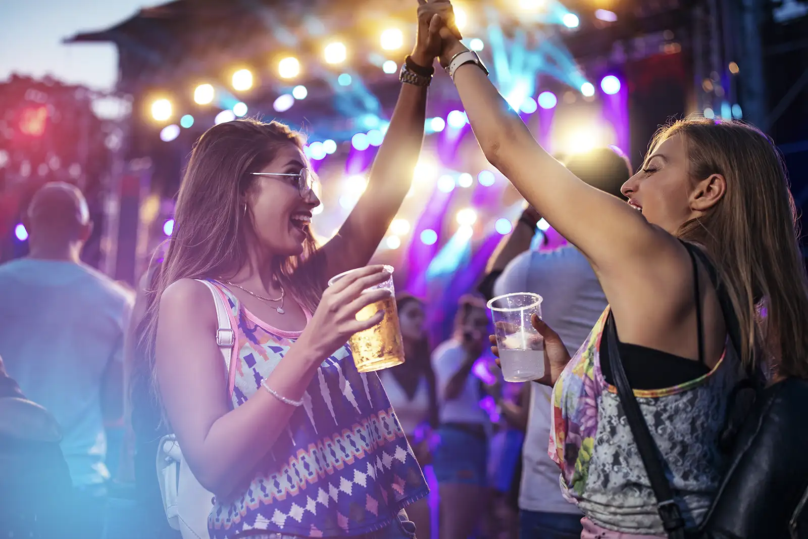 Two girls high fiving while holding beer and cocktails at an outdoor concert