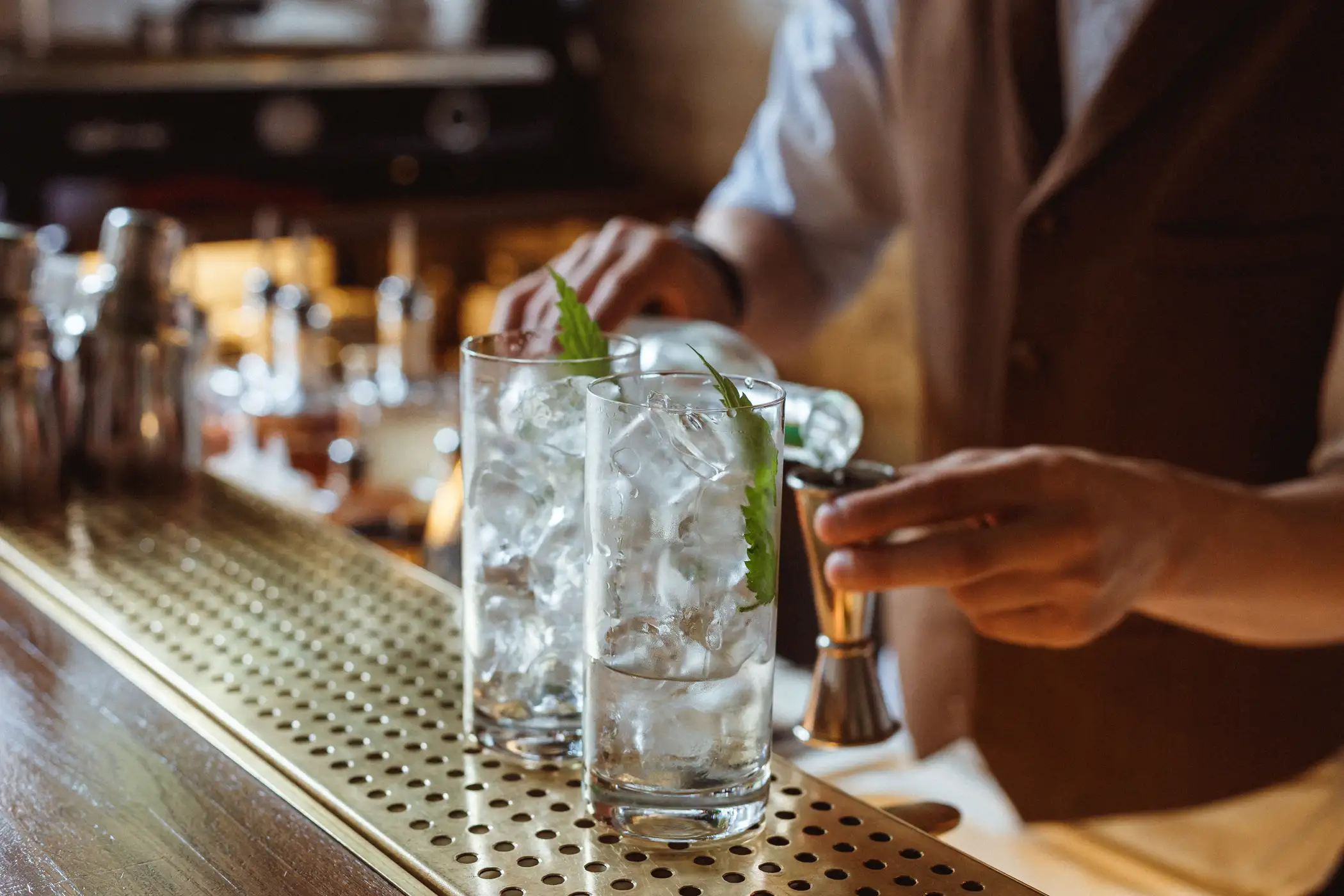 A bartender finishing two mixed drink cocktails with lime garnishes