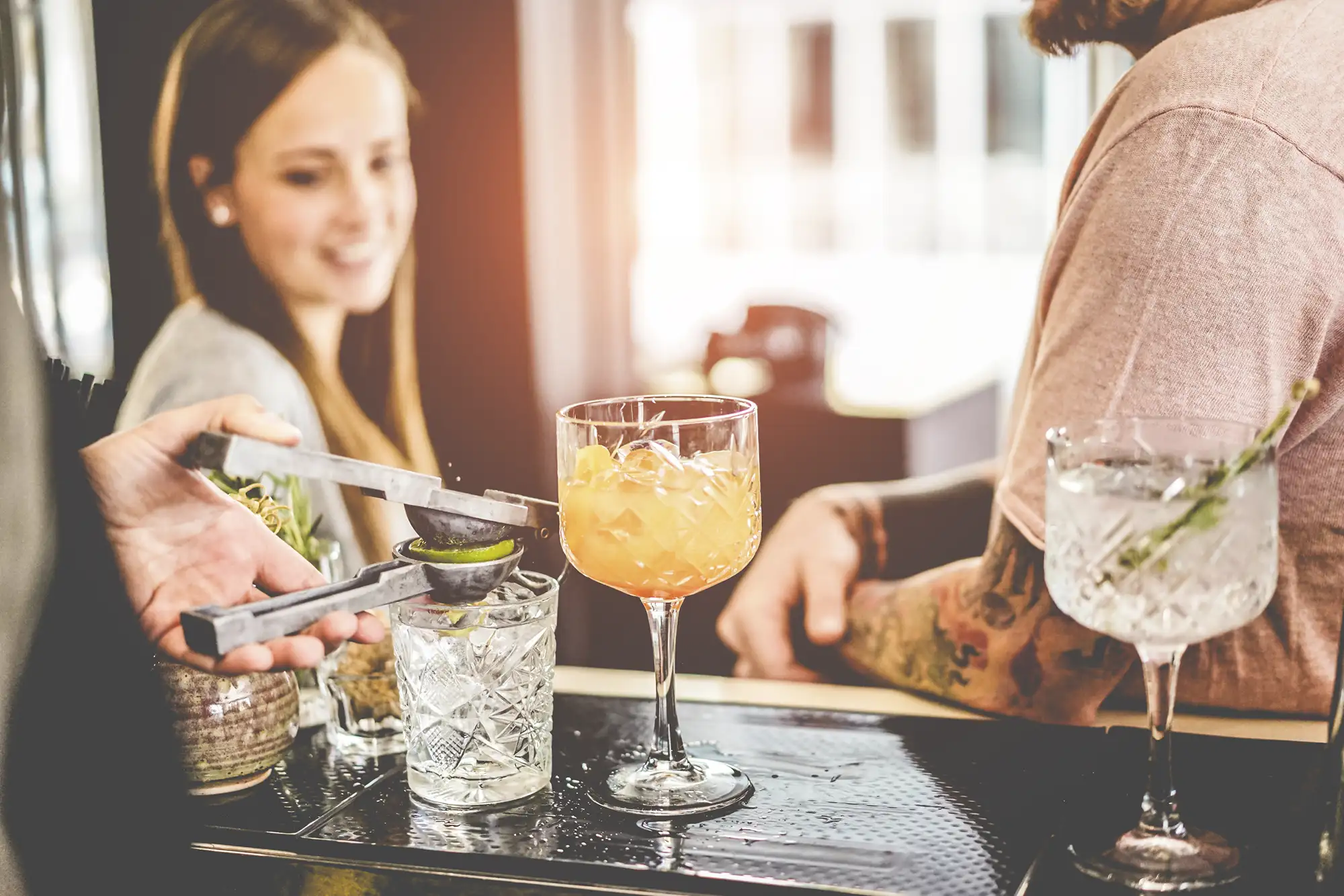 Couple sits at a bar while a bartender extracts lime juice for a cocktail mixed drink